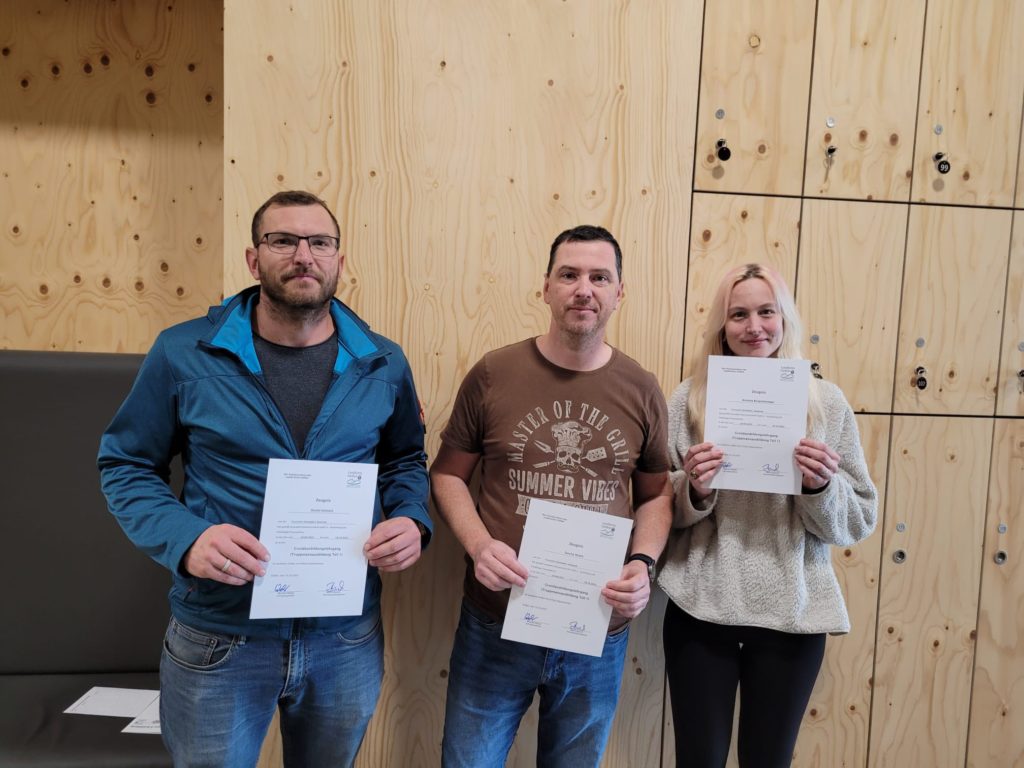 Drei Personen mit einer Teilnehmerurkunde der bestandenen Grundausbildung