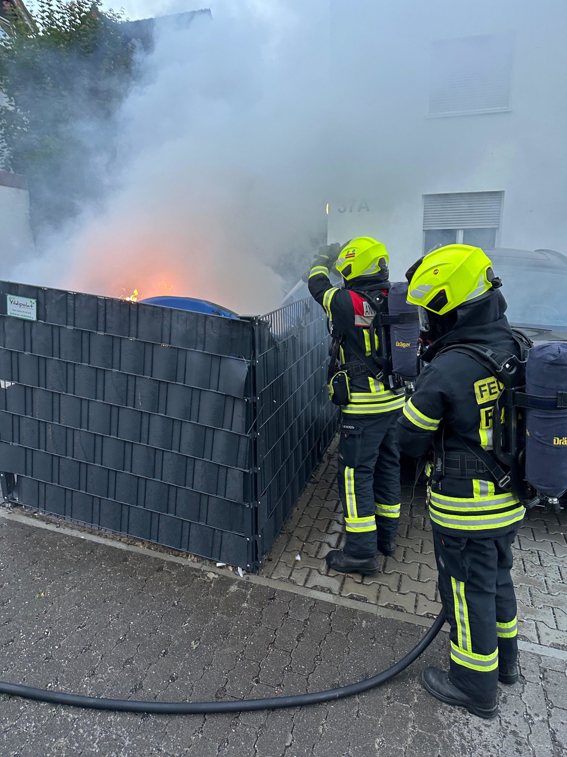 Zwei Einsatzkräfte in Schutzausrüstung bei der Bekämpfung eines Brandes einer Mülltonne
